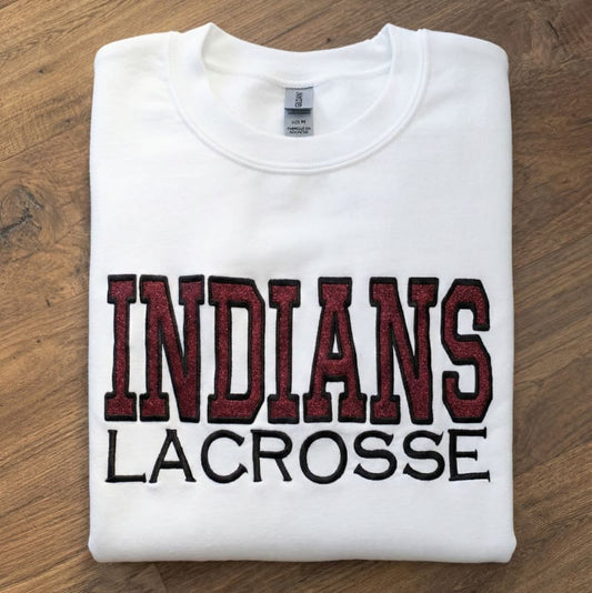 Folded white sweatshirt with 'INDIANS LACROSSE' text on a wooden surface